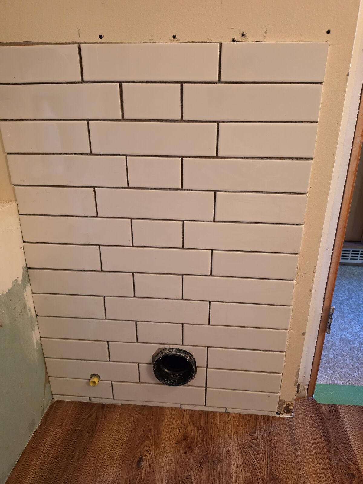 Close-up of new subway tile with toilet drain and water line ready for installation